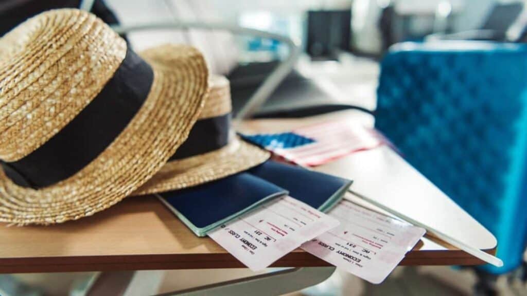 Two straw hats, passports, and boarding passes rest on a table with a blue suitcase and small American flag in the background—capturing the excitement of cruise ship embarkation and disembarkation adventures ahead.