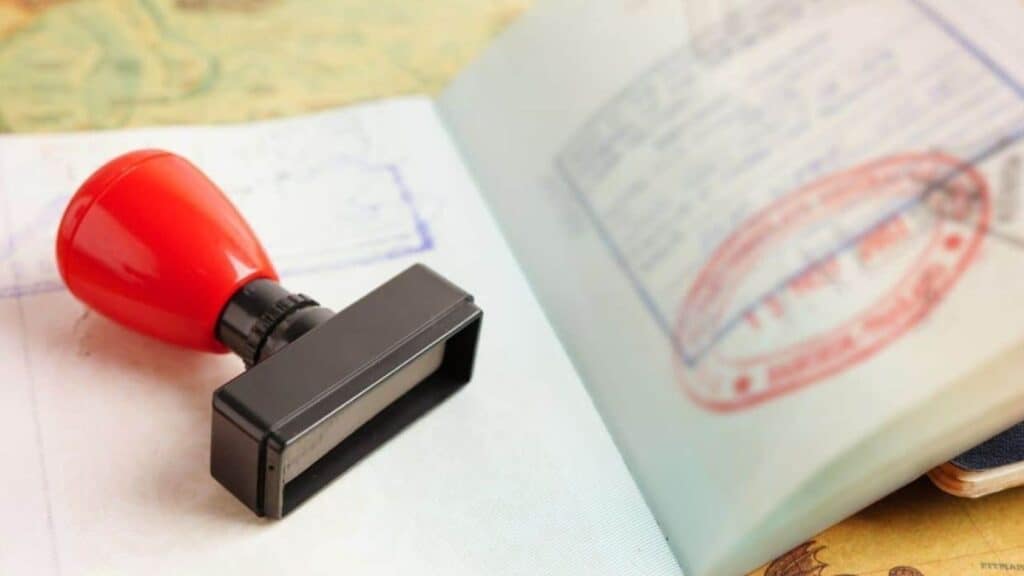 A red-handled rubber stamp rests on an open passport showing immigration stamps and official markings, serving as a reminder to always check passport validity rules before traveling.