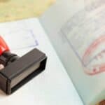 A red-handled rubber stamp rests on an open passport showing immigration stamps and official markings, serving as a reminder to always check passport validity rules before traveling.