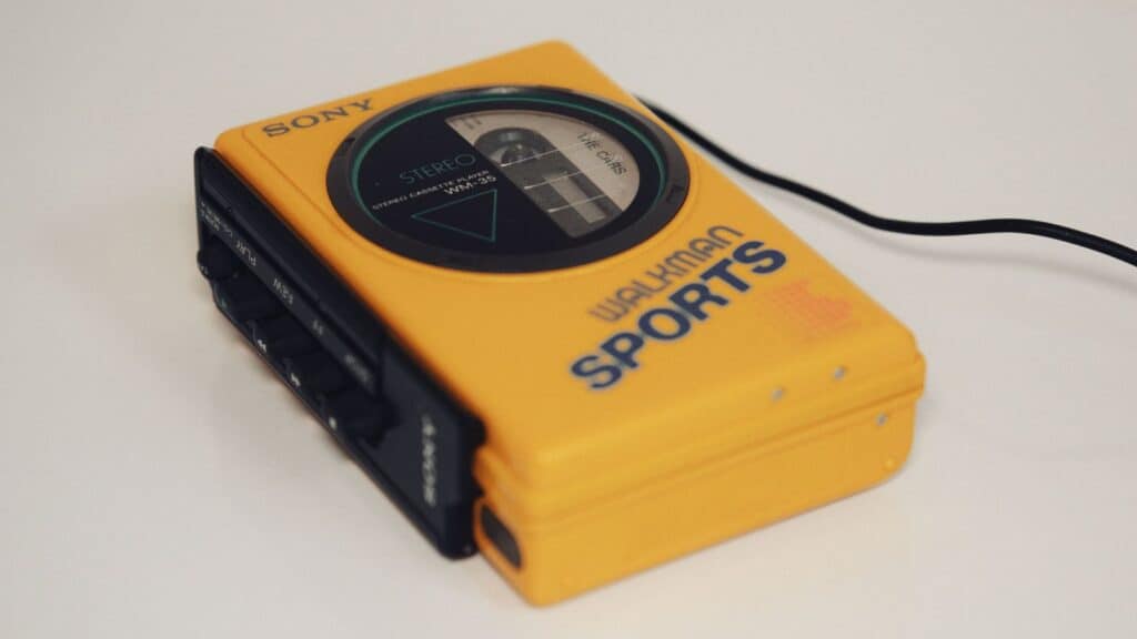 Yellow Sony Walkman Sports portable cassette player with black buttons and a partially visible cassette tape inside, resting on a white surface&mdash;a classic design that any Walkman owner remembers listening to music with during the golden age of cassettes.