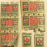 Six vintage trading S&H Green Stamps by Sperry and Hutchinson, four marked &ldquo;10 STAMPS&rdquo; and two marked &ldquo;50 STAMPS,&rdquo; are arranged on a plain surface.
