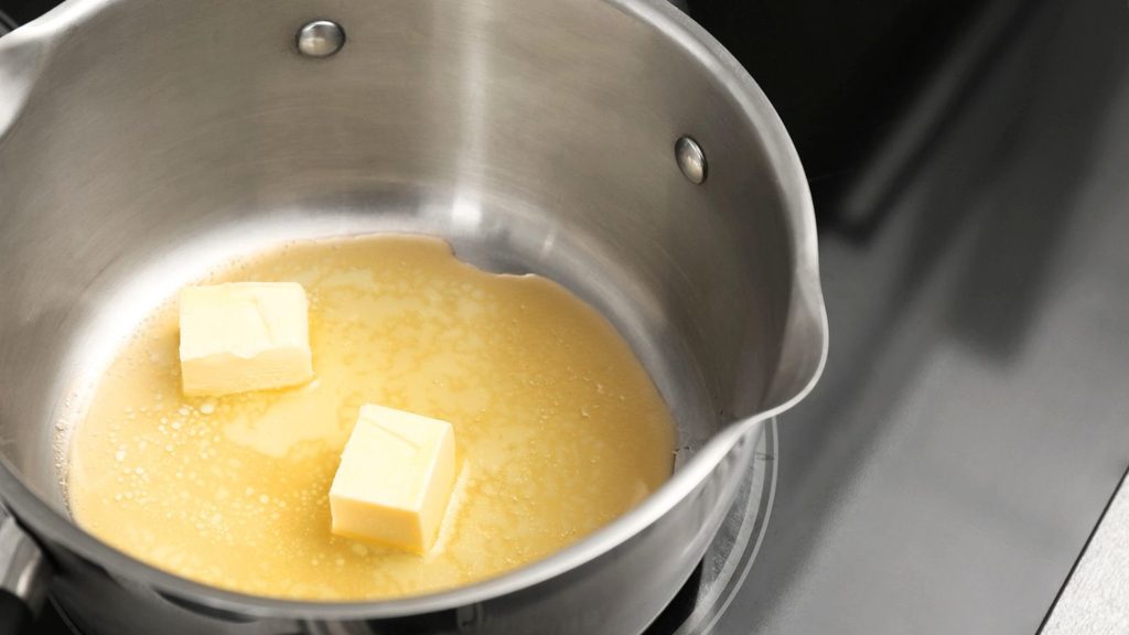 Two cubes of butter are partially melted in a stainless steel saucepan on a stovetop, beginning to transform into rich, fragrant brown butter.
