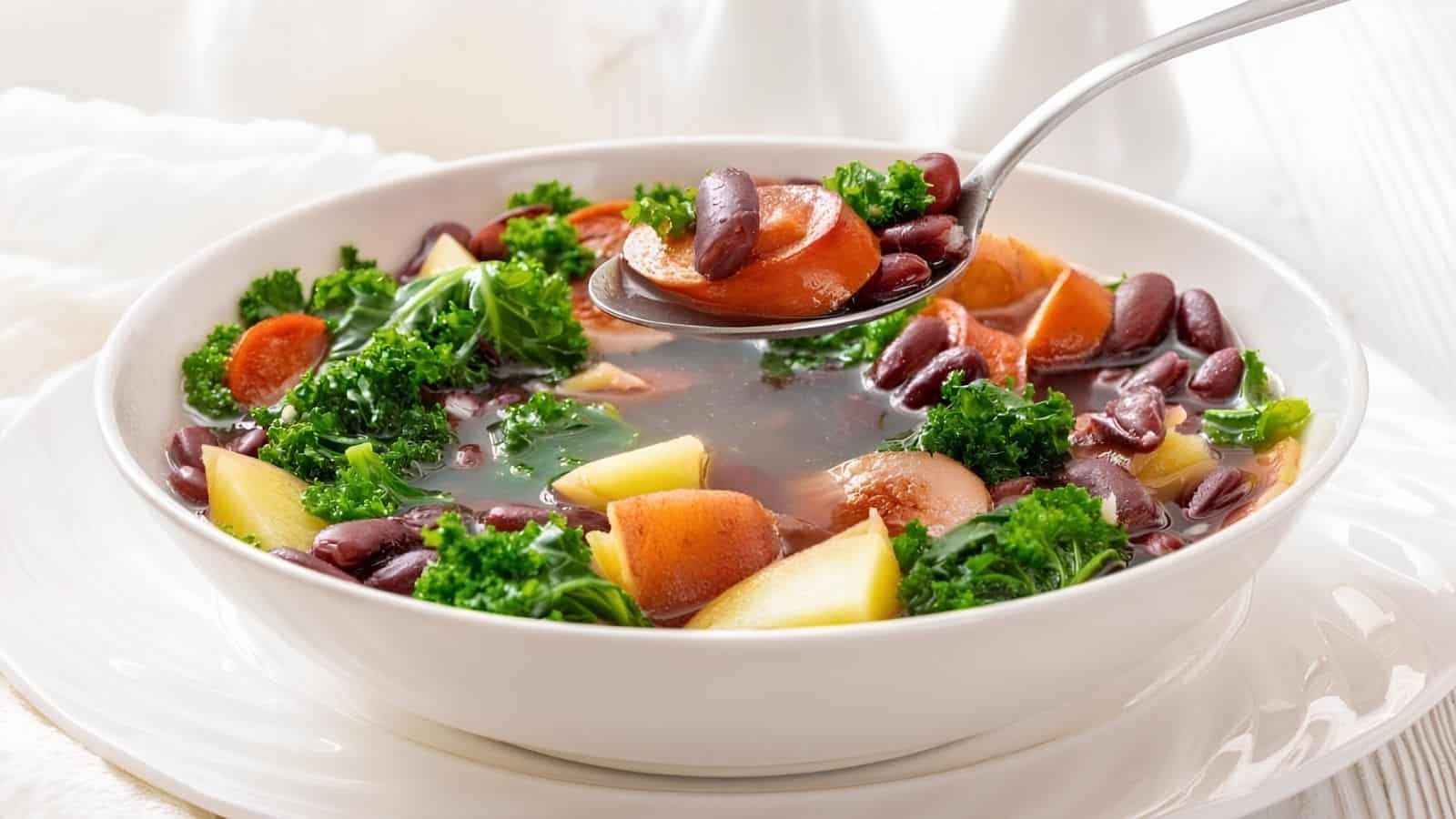 A bowl of Sausage & Kale Soup with a spoon lifting a portion from the bowl.