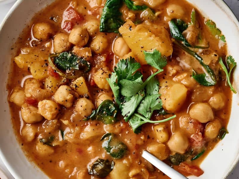 Bowl of chickpea stew with spinach, potatoes, tomatoes, and topped with fresh cilantro.