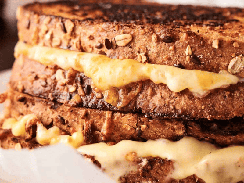 Close-up of two grilled cheese sandwiches on whole grain bread with melted cheese oozing out between the toasted slices.