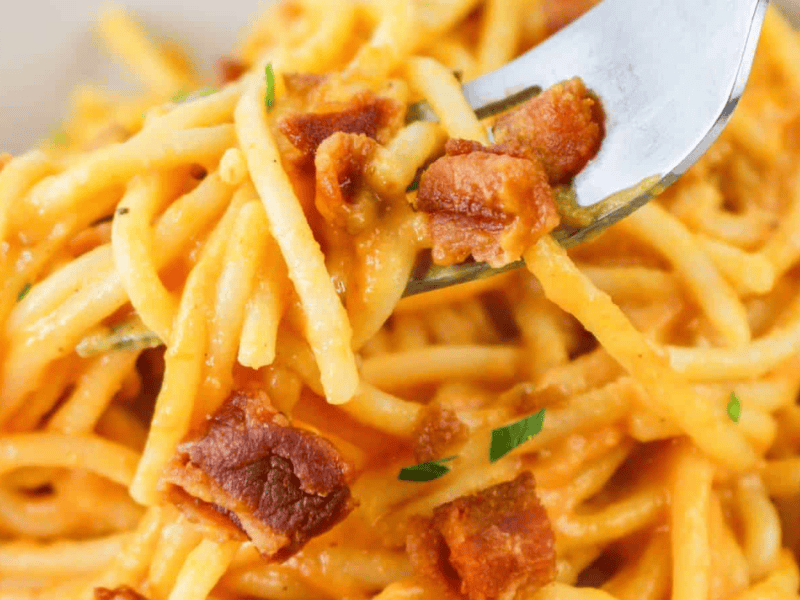 A close-up of a forkful of spaghetti carbonara with crispy bacon bits and garnished with green herbs.