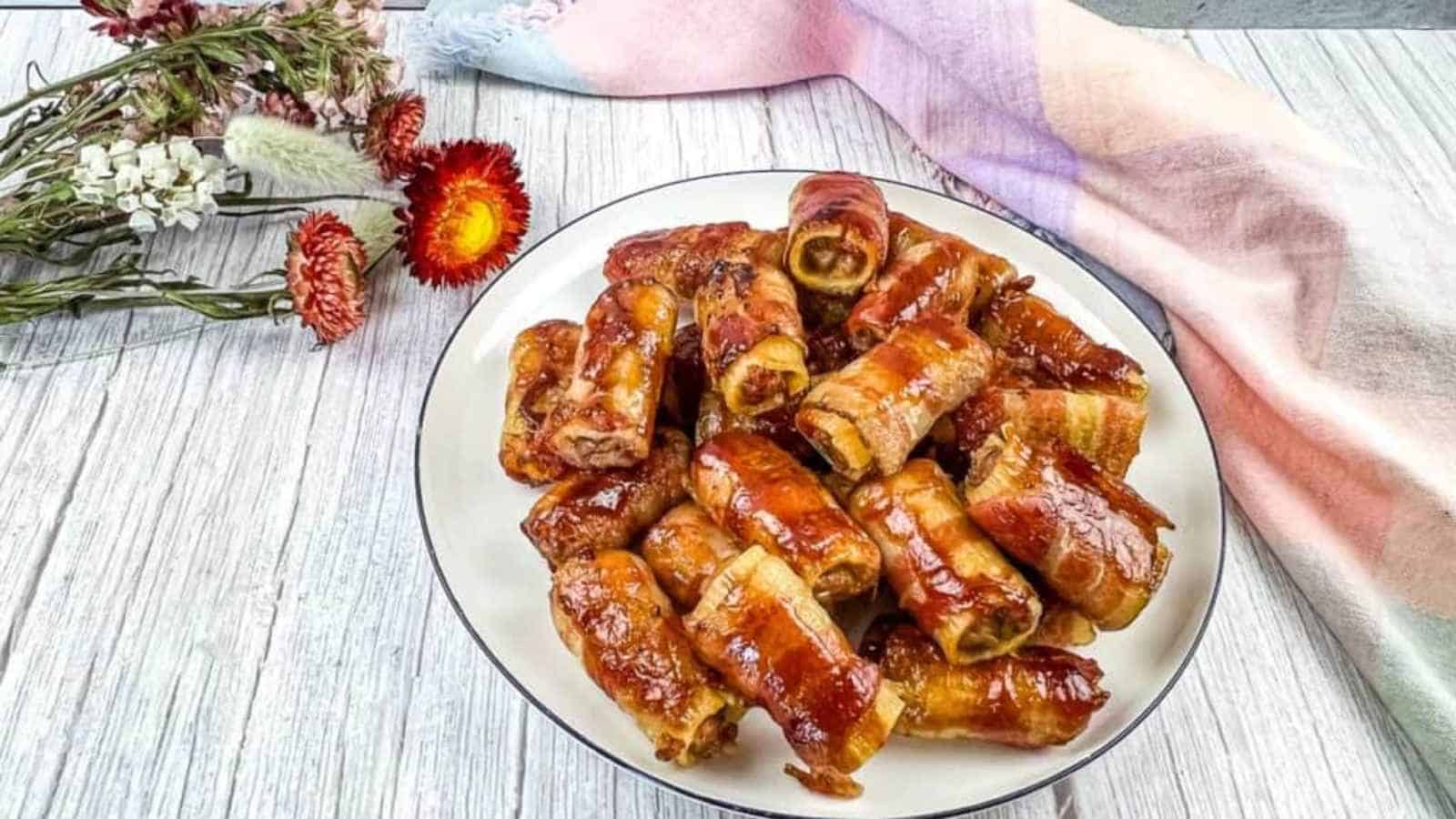 A plate of bacon-wrapped appetizers glazed in sauce.
