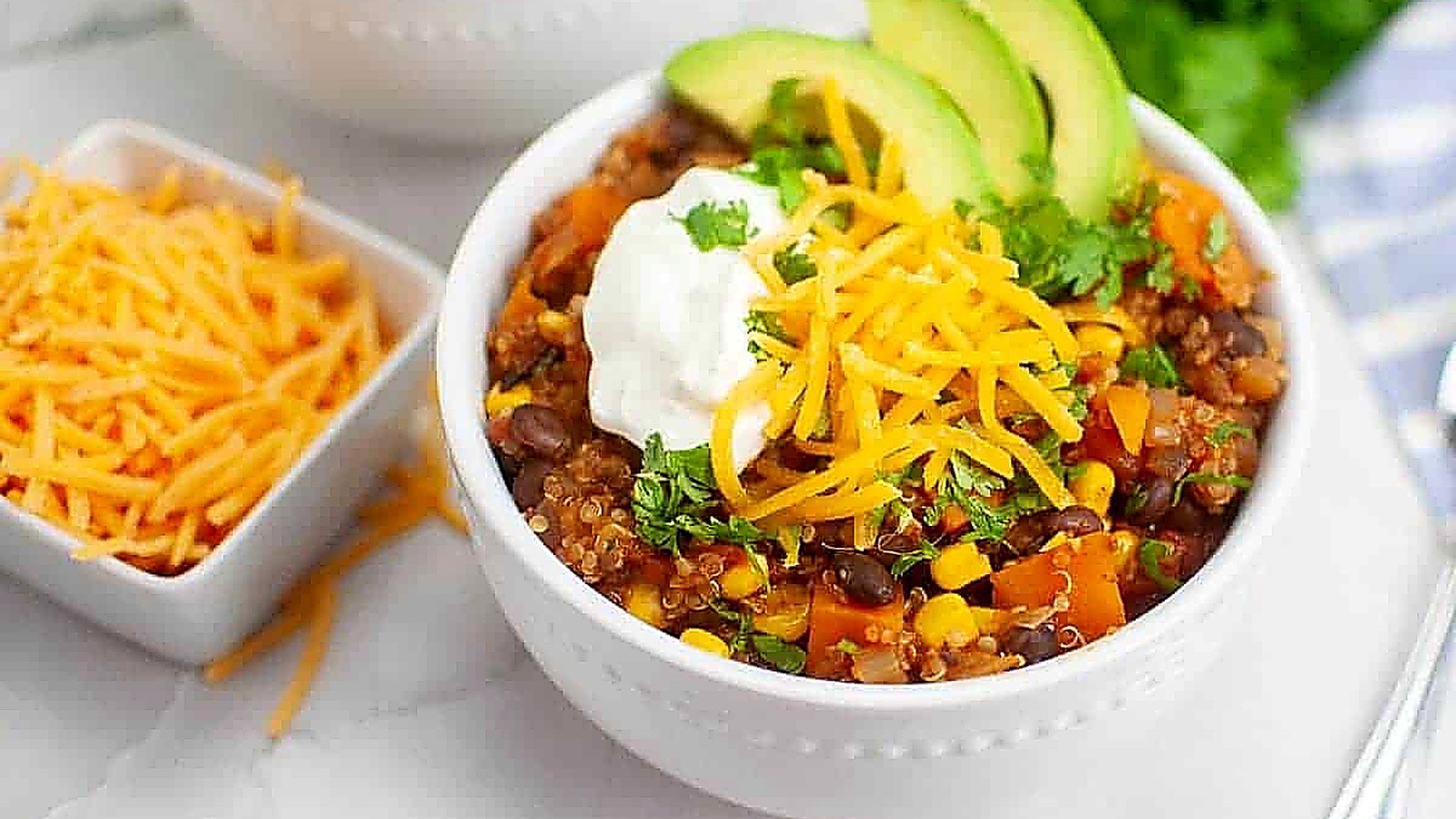 Two bowls of quinoa salad topped with avocado slices, cheese, and sour cream.