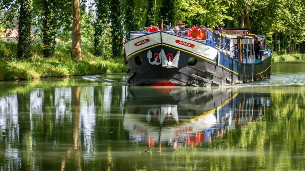 The barge named Rosa cruising through a tree-lined canal in Gascony, France.