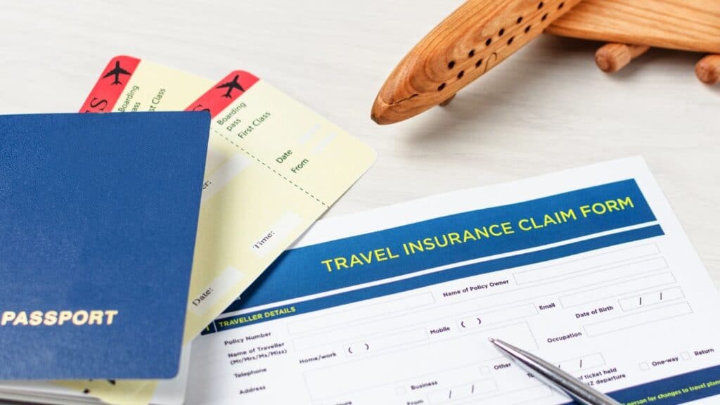 A passport, flight tickets, and a travel insurance claim form with a pen and a wooden airplane model on a light surface, illustrating the importance of understanding what travel insurance does not cover before your trip.