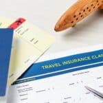 A passport, flight tickets, and a travel insurance claim form with a pen and a wooden airplane model on a light surface, illustrating the importance of understanding what travel insurance does not cover before your trip.