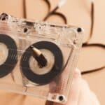 Close-up of hands rewinding a cassette tape with a pencil, evoking classic mixtape making teenager rituals, with some of the tape unraveled in the background.
