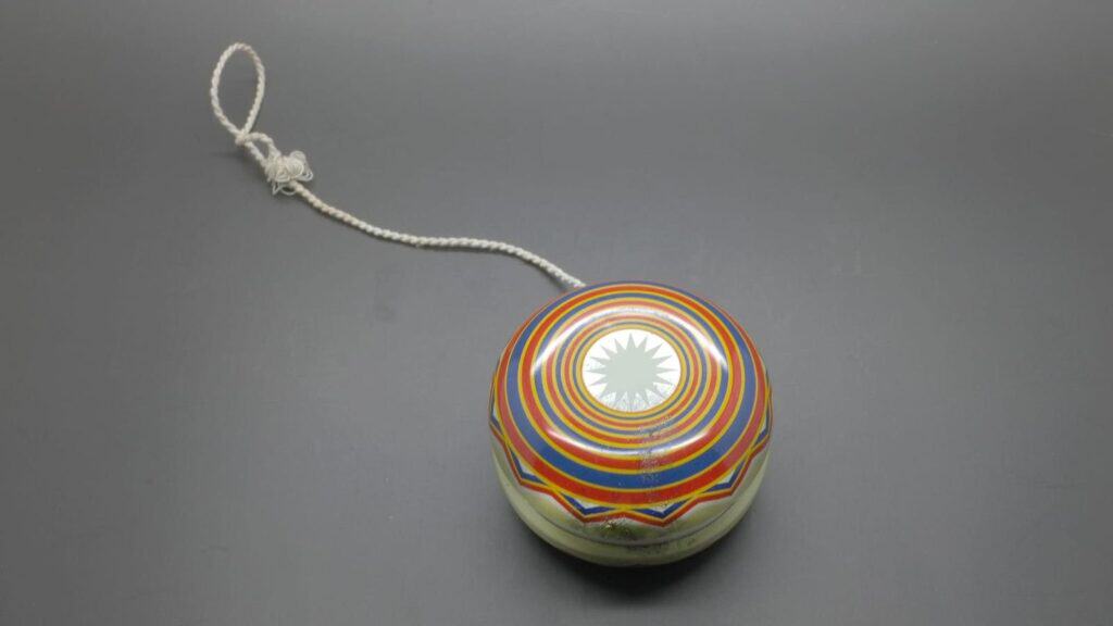 A metal yo-yo with a multicolored geometric design and a string attached, placed on a plain gray surface, evokes memories of playground fads that ruled recess.