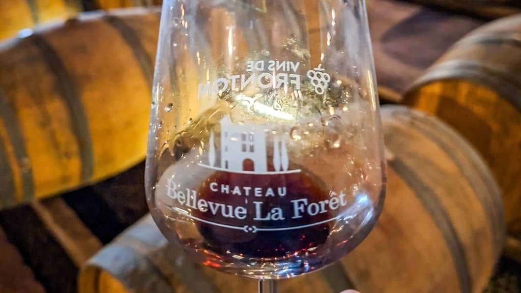 A glass of Chateau Bellevue La For&ecirc;t red wine sits in a Gascony, France wine cellar among wooden barrels.