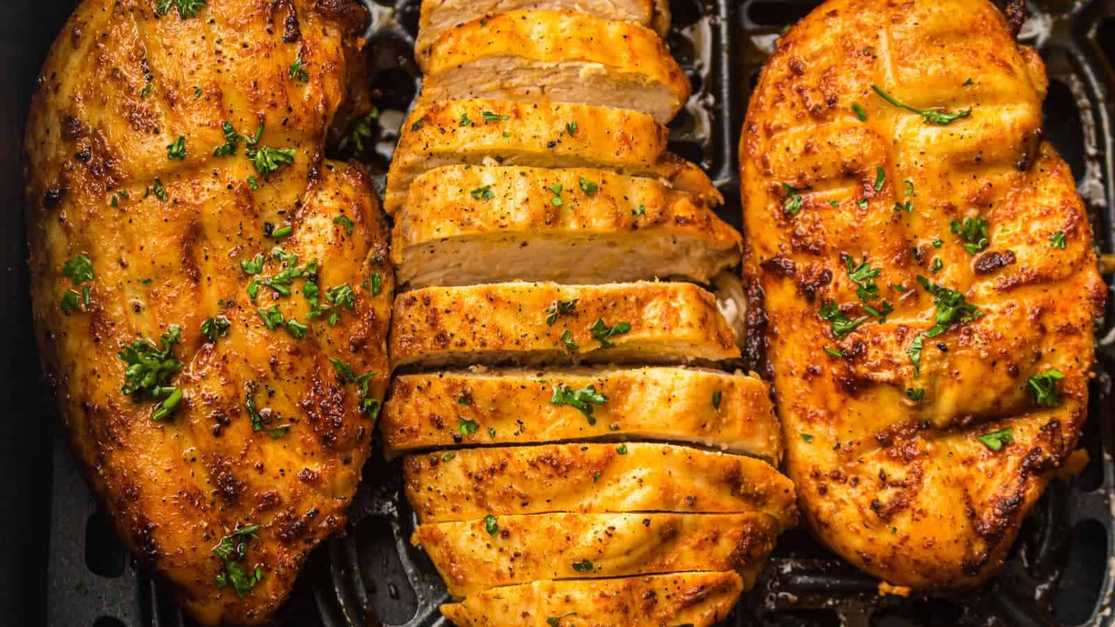 Sliced grilled chicken breast seasoned with herbs and pepper, displayed on an air fryer tray.