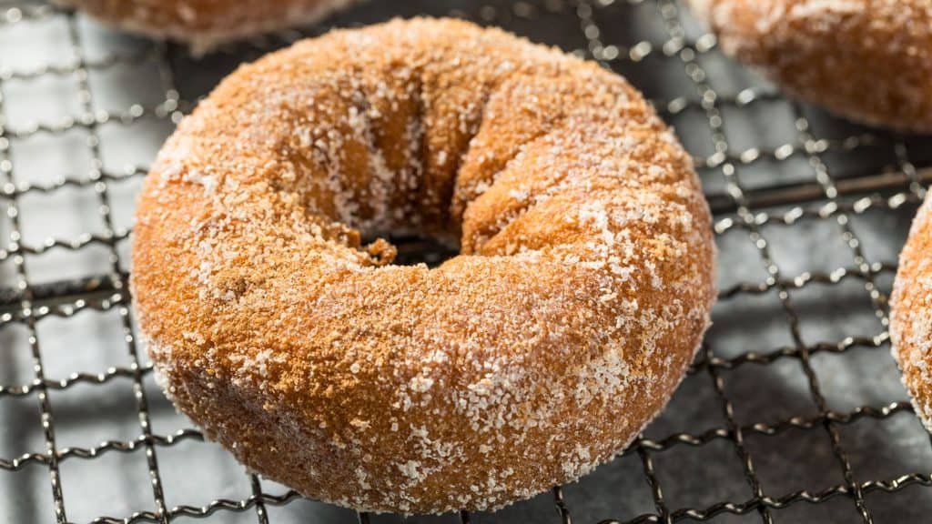 A close-up of an apple cider donut, generously coated in sugar, resting on a metal cooling rack.