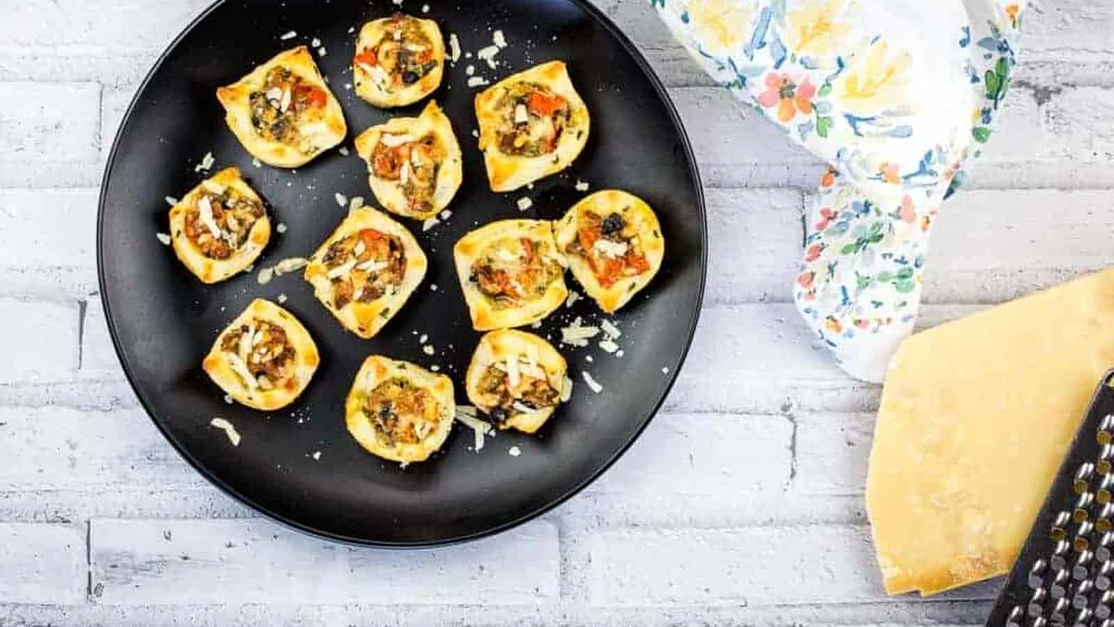 A black plate with bacon and mushroom tartlets on it.
