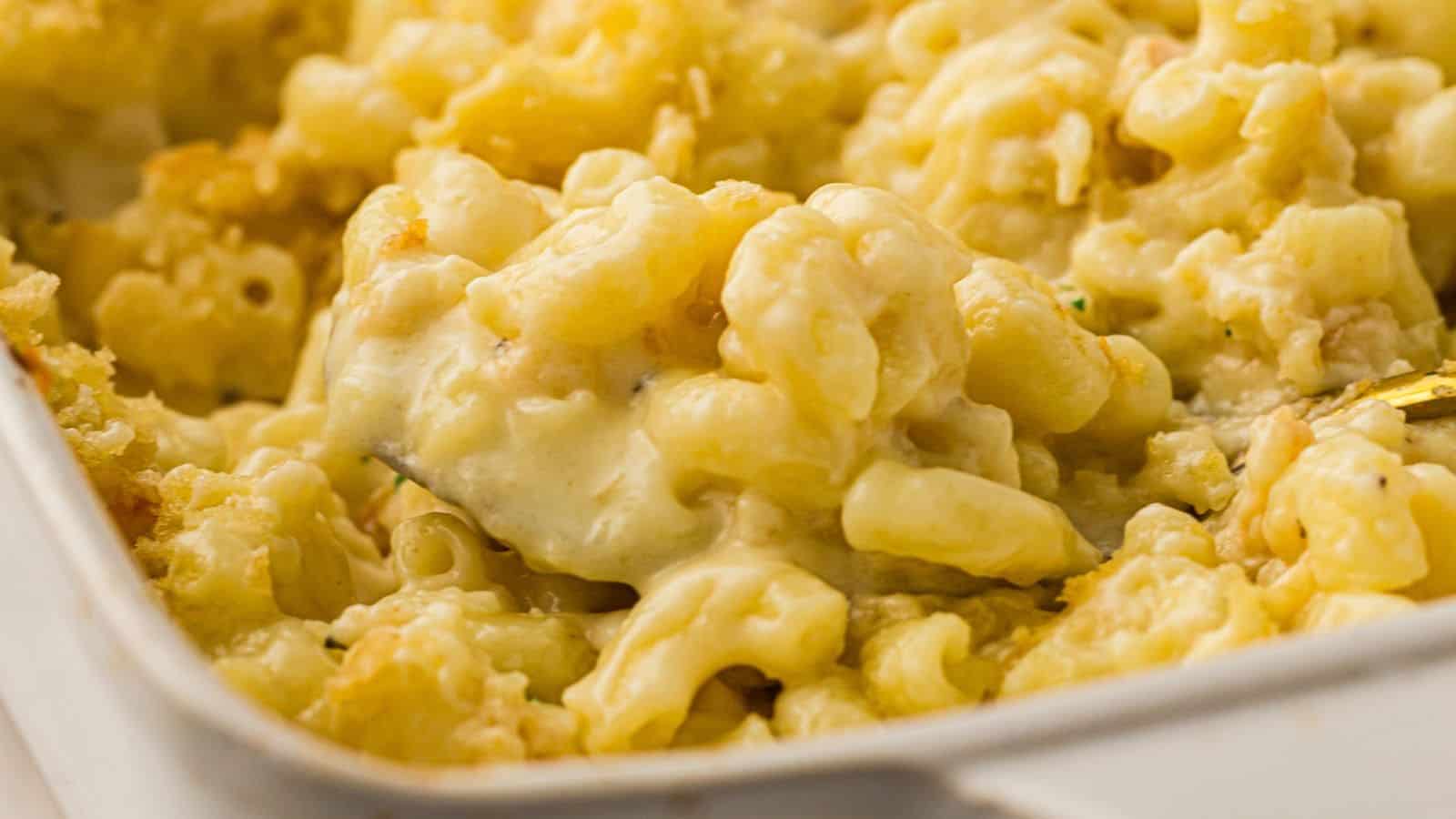 Close-up of creamy baked macaroni and cheese in a white dish, with a serving spoon lifting a portion.