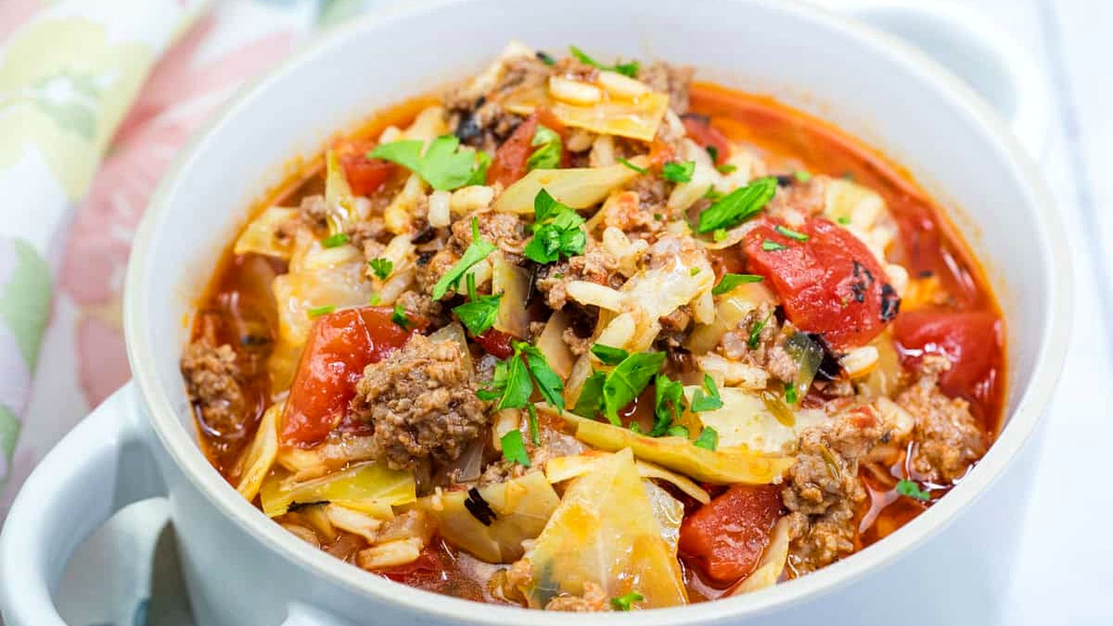 A bowl of cabbage roll soup with ground meat, chopped tomatoes, and rice, garnished with fresh parsley.
