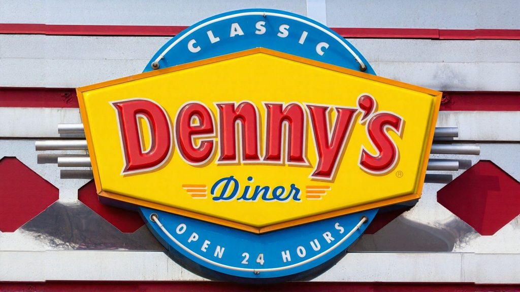 A Denny&rsquo;s Diner sign with yellow, red, and blue colors reads &ldquo;Classic Denny&rsquo;s Diner Open 24 Hours,&rdquo; mounted on a building exterior.