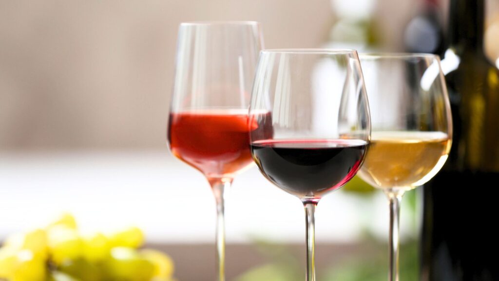 Three wine glasses are arranged side by side, each containing a different type of wine&mdash;ros&eacute;, red, and white&mdash;in preparation for the Somm Smackdown 2026. A blurred bottle and yellow object appear in the background.