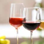 Three wine glasses are arranged side by side, each containing a different type of wine—rosé, red, and white—in preparation for the Somm Smackdown 2026. A blurred bottle and yellow object appear in the background.