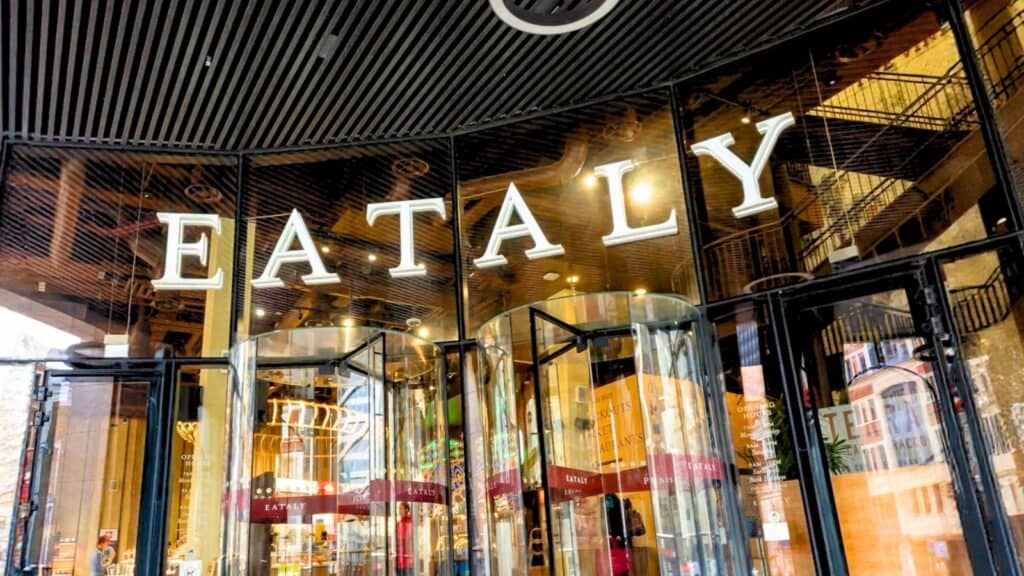 The front entrance of Eataly, with large glass revolving doors and the store name in bold white letters above the doorway, offers a grand welcome for guests exploring luxury hotels near food halls.