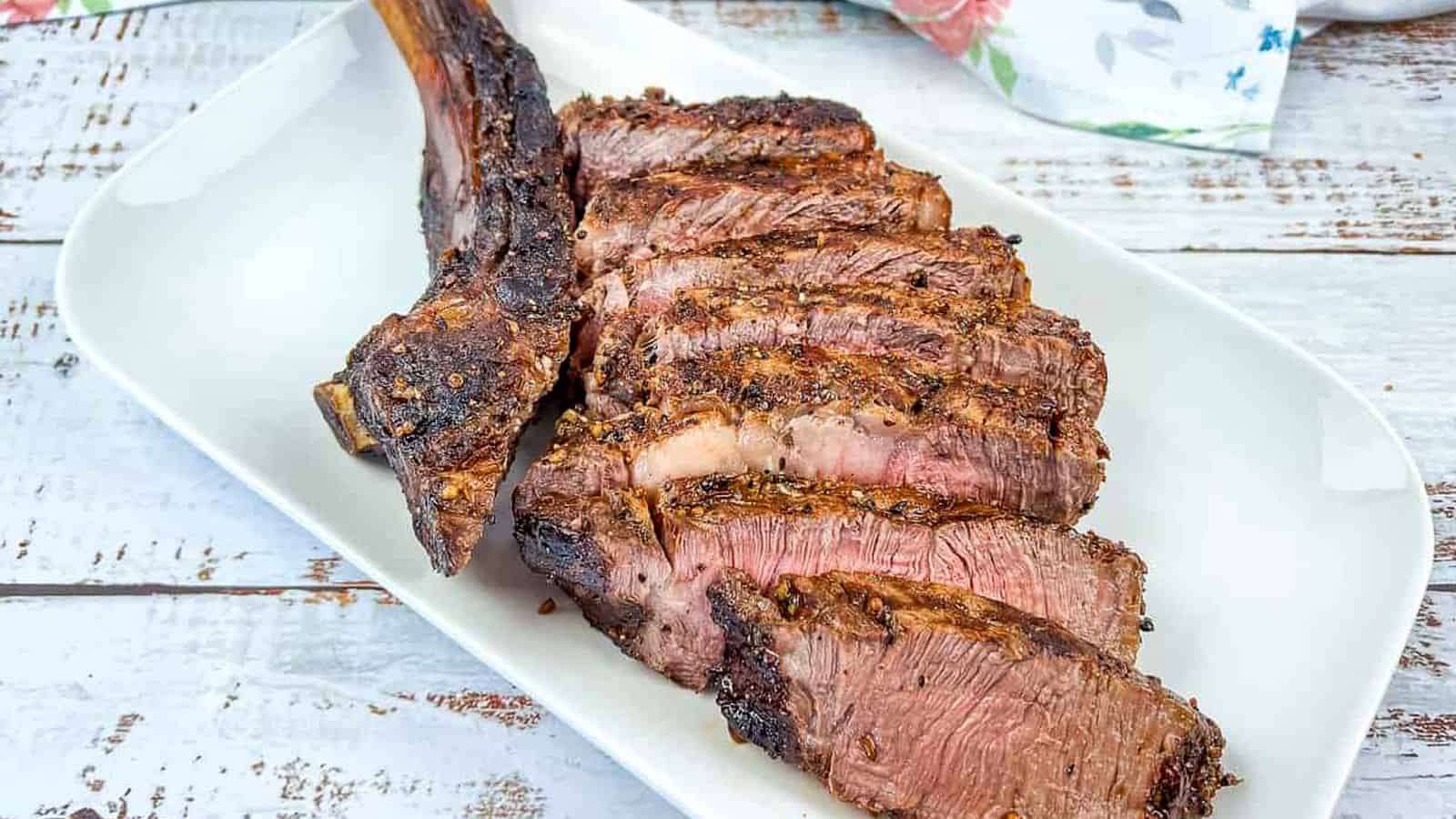 A sliced tomahawk steak on a white plate.