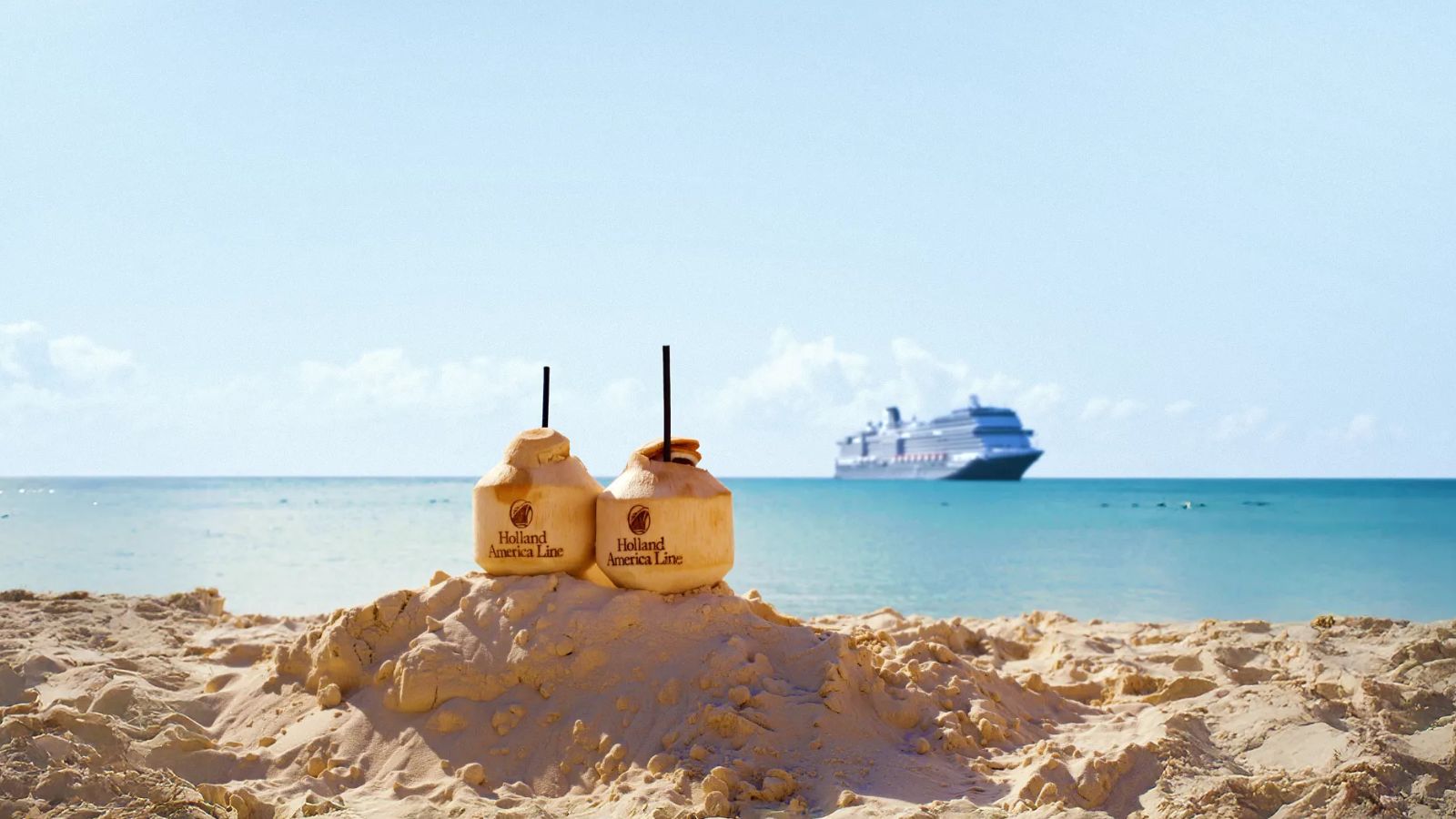 Two coconuts with straws on sandy beach, cruise ship in the background on calm blue ocean under a clear sky.
