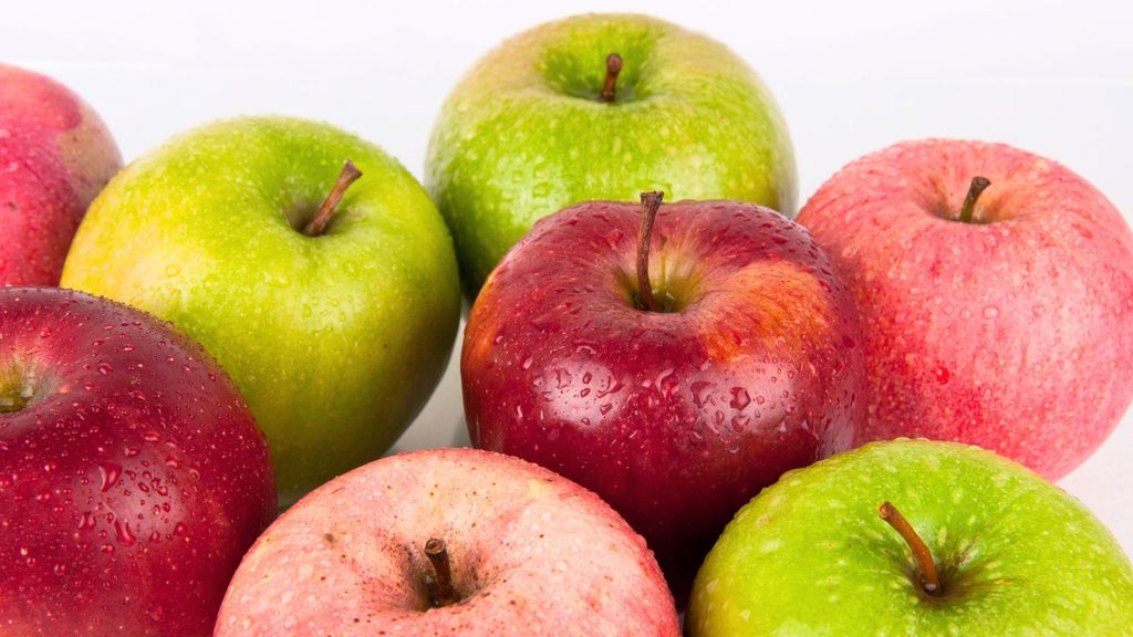 A close-up of several red and green apples with water droplets on their skin, grouped together against a white background&mdash;perfect for those wondering what are the best apples for baking.