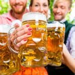 Five people in traditional Bavarian clothing hold large beer mugs, toasting together outdoors at Oktoberfest.