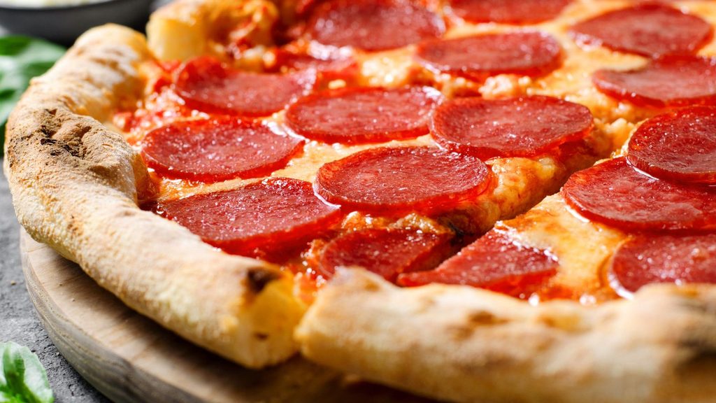 A close-up of a pepperoni pizza with melted cheese and a thick, golden-brown crust, sliced and served on a wooden board.
