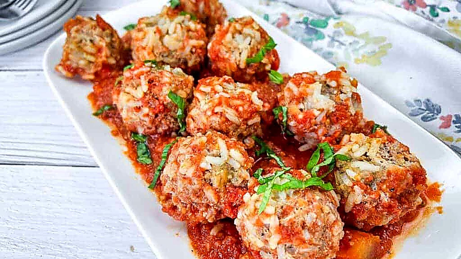 A white rectangular plate with slow cooker porcupine meatballs, garnished with fresh herbs.