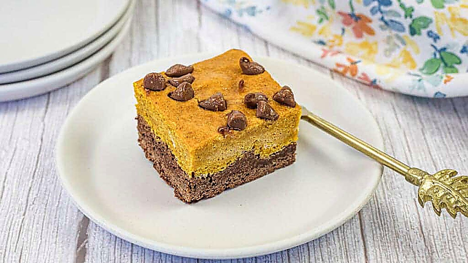 A square piece of pumpkin brownies sprinkled with chocolate chips, placed on a white plate.