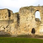 Stone ruins of Reading Abbey with arched windows and doorways, weathered walls, and patches of grass in the foreground under a partly cloudy sky.