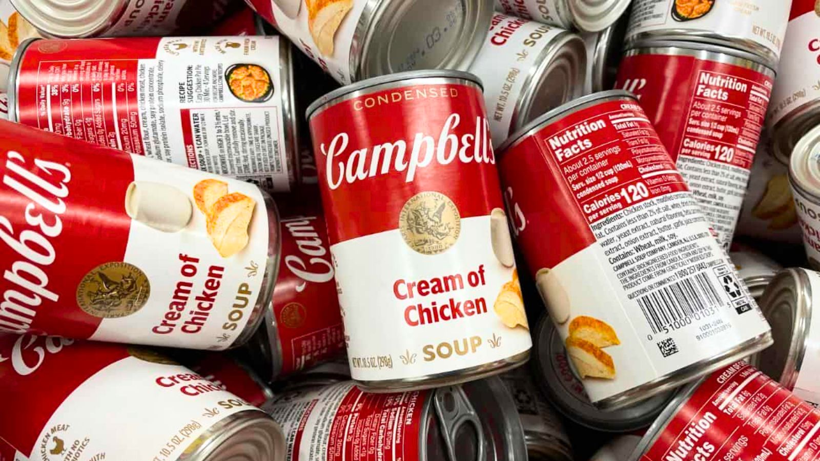 Several cans of Campbell&rsquo;s Cream of Chicken Soup are closely stacked, showing the red and white labels, product name, and some nutrition information on the back.