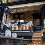 A house porch decorated for Halloween with skulls, fake cobwebs, tombstones, hanging ghouls, and orange pumpkin decorations.