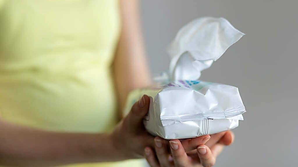 A person in a yellow shirt holds an open pack of wipes with one wipe partially pulled out.