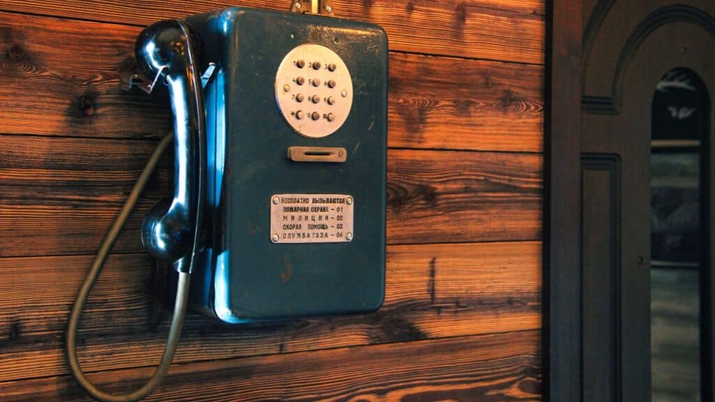 Blue wall-mounted public telephone with a keypad and an instruction plate listing emergency numbers, a landline phone feature unfamiliar to many younger generations.