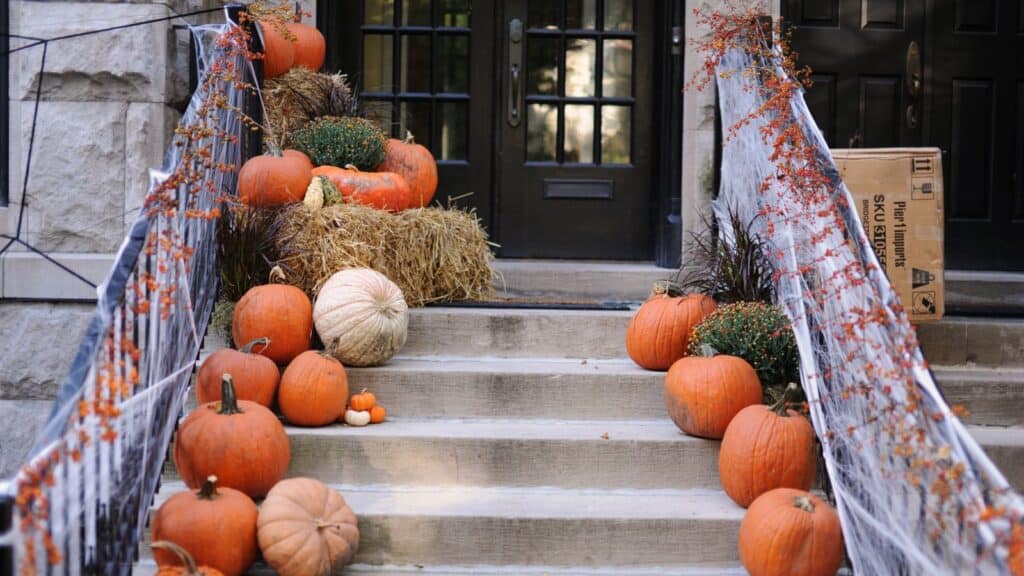 Front steps decorated with pumpkins, hay bales, and faux spiderwebs as porch fixes before trick-or-treaters arrive for Halloween.