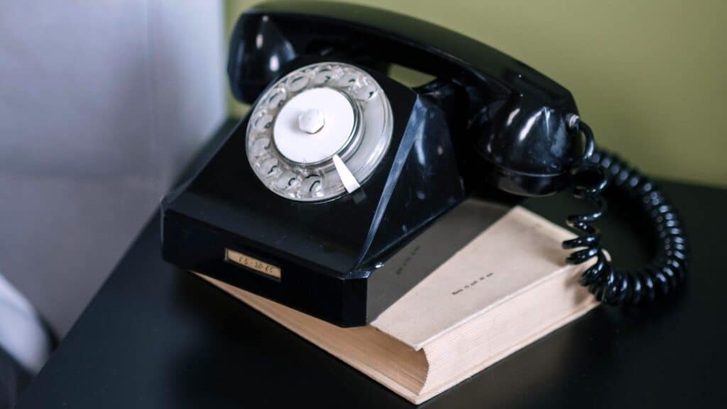 A black rotary telephone, often unfamiliar to younger generations, sits on top of a closed book.