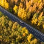 An aerial view of a car on a road trip through a forest with vibrant fall foliage.