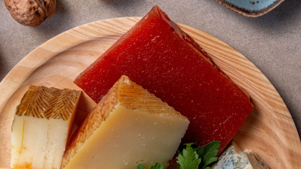 A wooden platter holding a large block of red quince paste and wedges of various cheeses, perfect for fall cheese pairings.