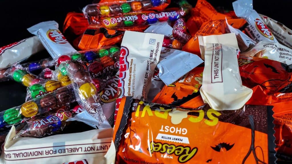 A pile of assorted snack-sized candy bars, including Kit Kat, Sixlets, and Reese&rsquo;s ghosts, perfect for Halloween candy bowl tricks.
