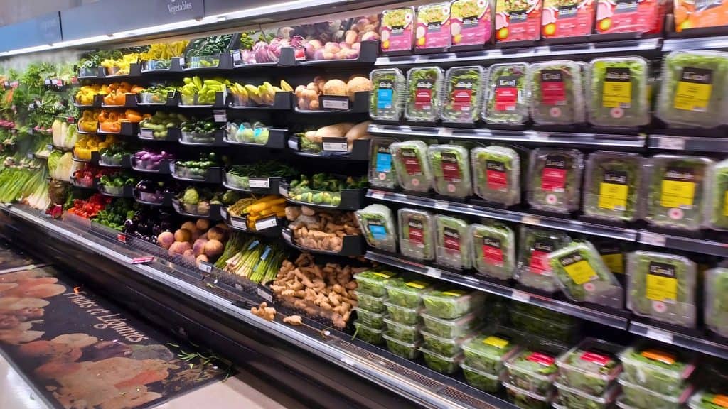 Produce section in a grocery store with shelves of fresh vegetables and rows of packaged salad greens.