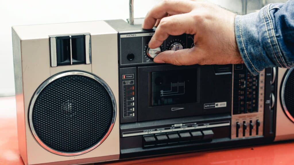 A hand adjusting the volume knob on a vintage portable cassette player, evoking boom box memories.