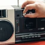 A hand adjusting the volume knob on a vintage portable cassette player, evoking boom box memories.