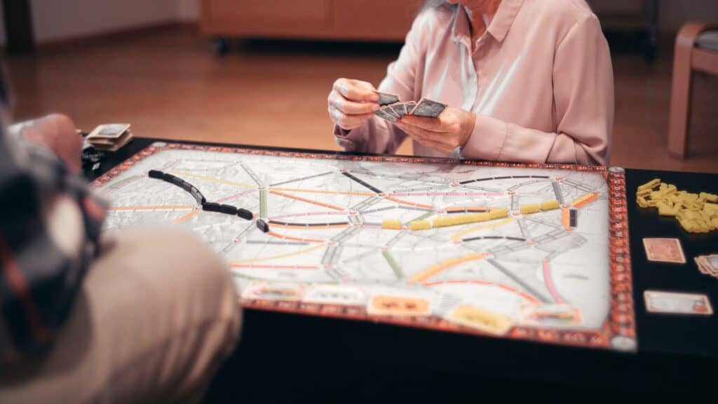 Two people playing a fall board game featuring plastic trains on a map.