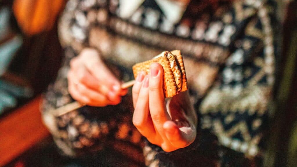 A person holding a s&rsquo;more on a wooden skewer, perfect for fall-themed hotel packages.