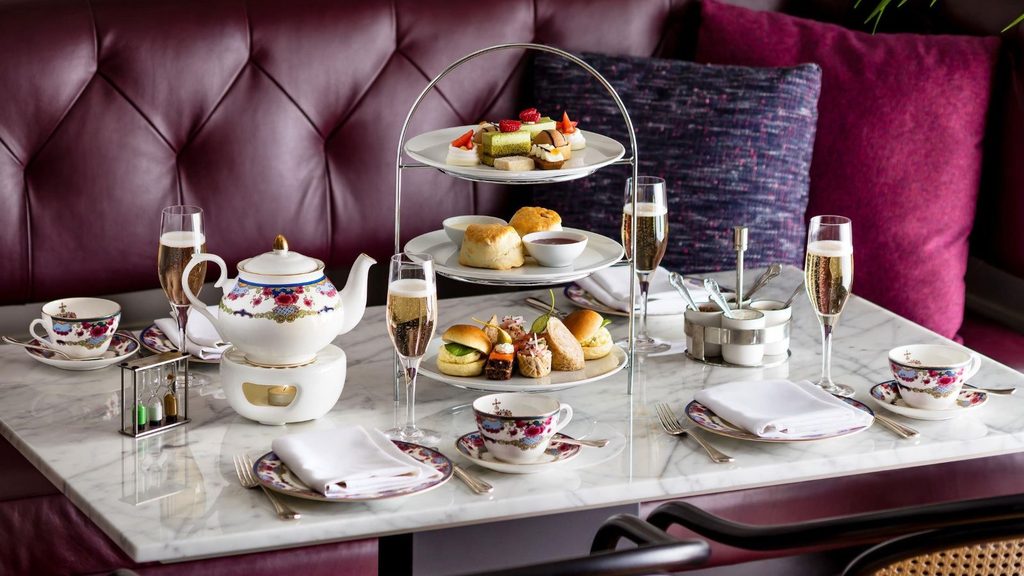 A three-tier Fairmont Empress afternoon tea service featuring finger sandwiches, scones, and small desserts, accompanied by a teapot and glasses of champagne on a marble table.